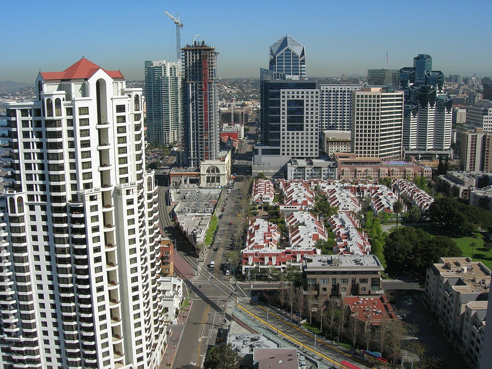 Downtown from above, a tower under construction at center and One America Plaza behind it, with trolley tracks and city streets below. Streets, sidewalks, facilities and fleet all sat in Bezak's most recent portfolio as Chief Performance and Logistics Officer, and they stay at the center of the operating job she now holds.
